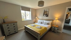 A bedroom with a bed, bedside tables, a window, a lamp, a painting, and a dresser. - The Clyde (Melrose)