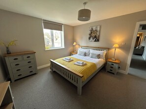 A bedroom with a bed, bedside tables, a window, a lamp, a painting, and a dresser. - The Clyde (Melrose)