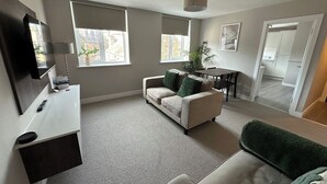 A modern living room with a sofa, a dining table, and a TV. - The Clyde (Melrose)