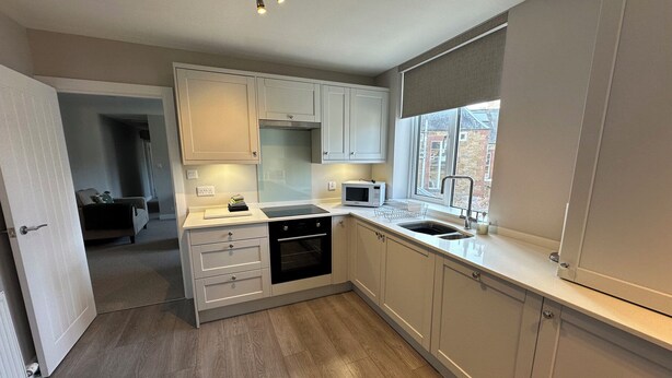 A modern kitchen with white cabinets, a built-in oven, a microwave, and a window with a view. - The Clyde (Melrose)