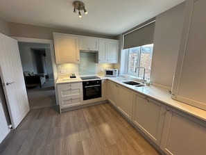 A modern kitchen with white cabinets, a built-in oven, a microwave, and a window with a view. - The Clyde (Melrose)