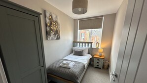 A bedroom with a bed, bedside table, lamp, window, and artwork. - The Clyde (Melrose)