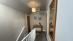 A hallway with a white railing, a ceiling fan, and a wooden door. - Pergola (Melrose)