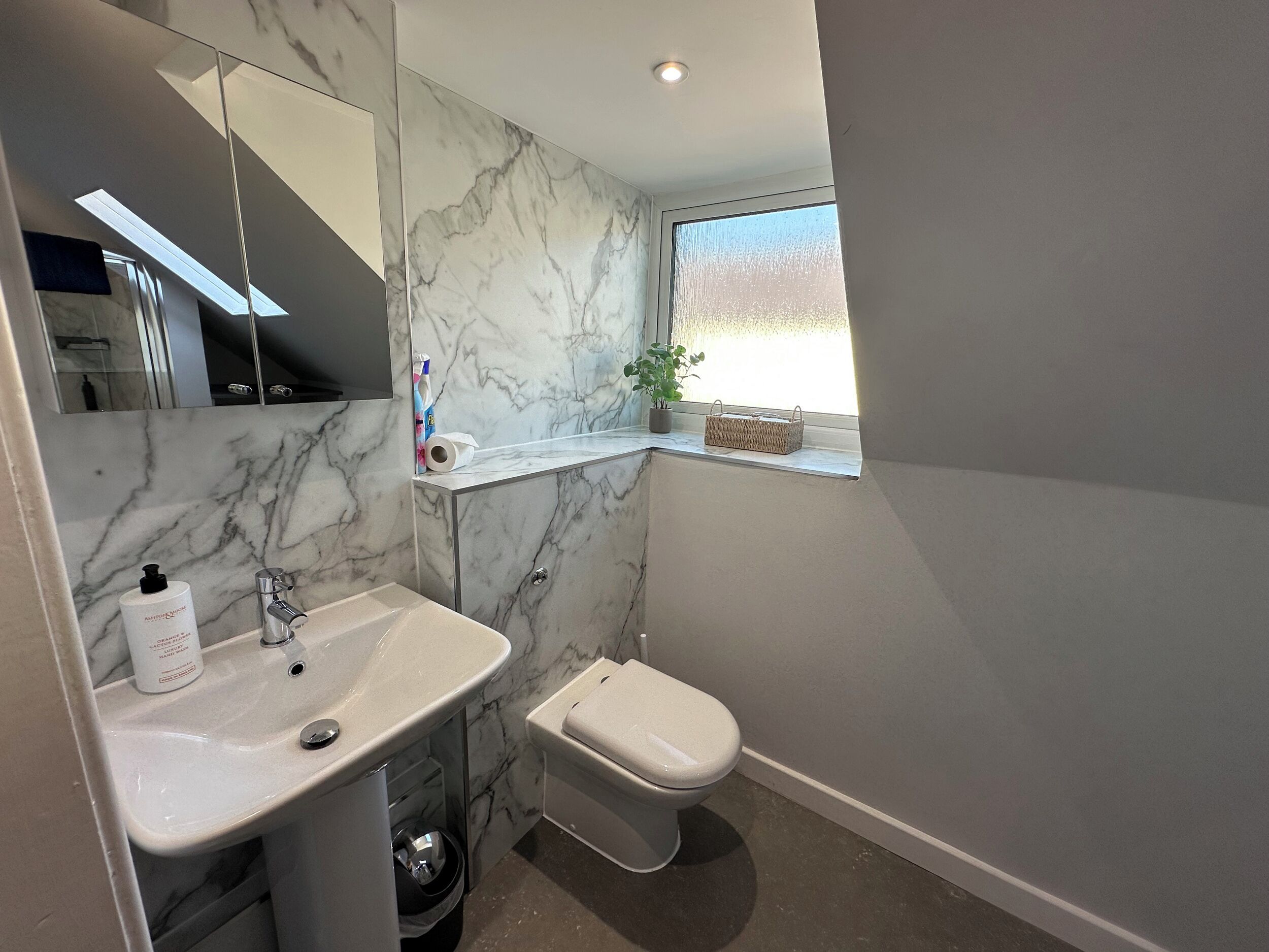 Une salle de bain avec un mur en marbre, un lavabo, des toilettes, un miroir et une fenêtre.