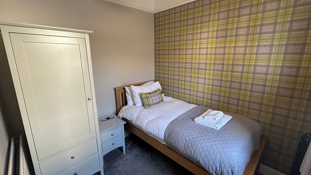 A bedroom with a bed, a nightstand, a wardrobe, and a plaid-patterned wall. - Pergola (Melrose)