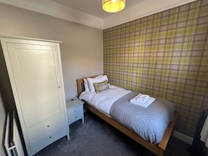 A bedroom with a bed, a nightstand, a wardrobe, and a plaid-patterned wall. - Pergola (Melrose)