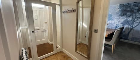 Un pasillo con un radiador, un espejo y una puerta que da a otra habitación.