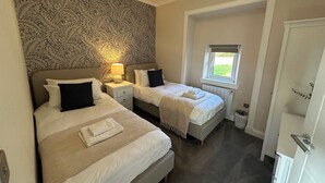 Et soveværelse med to senge, tapet med mønster, et vindue med udsigt og en loftlampe.