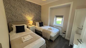 A bedroom with two beds, a patterned wallpaper, a window with a view, and a ceiling light.