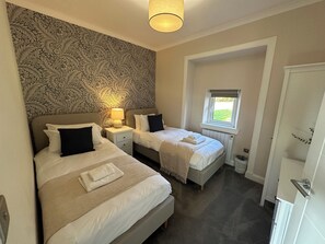 Ein Schlafzimmer mit zwei Betten, einer Wand mit Musterung, einem Fenster mit Ausblick und einer Deckenleuchte.