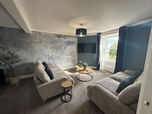 A living room with a sofa, armchair, round coffee table, and a potted plant. - Broombank (Melrose)