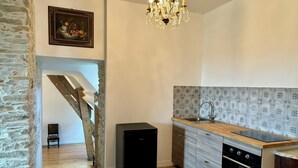 A kitchen with a stone wall, a chandelier, a refrigerator, a sink, and a patterned backsplash. - Château de la Pervenchère - Gîte des Cavaliers (Casson)