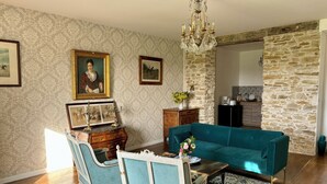 A living room with a teal sofa, a wooden cabinet, a chandelier, and a stone wall. - Château de la Pervenchère - Gîte des Cavaliers (Casson)