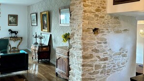 A room with a stone wall, wooden flooring, a chandelier, and a fireplace. - Château de la Pervenchère - Gîte des Cavaliers (Casson)