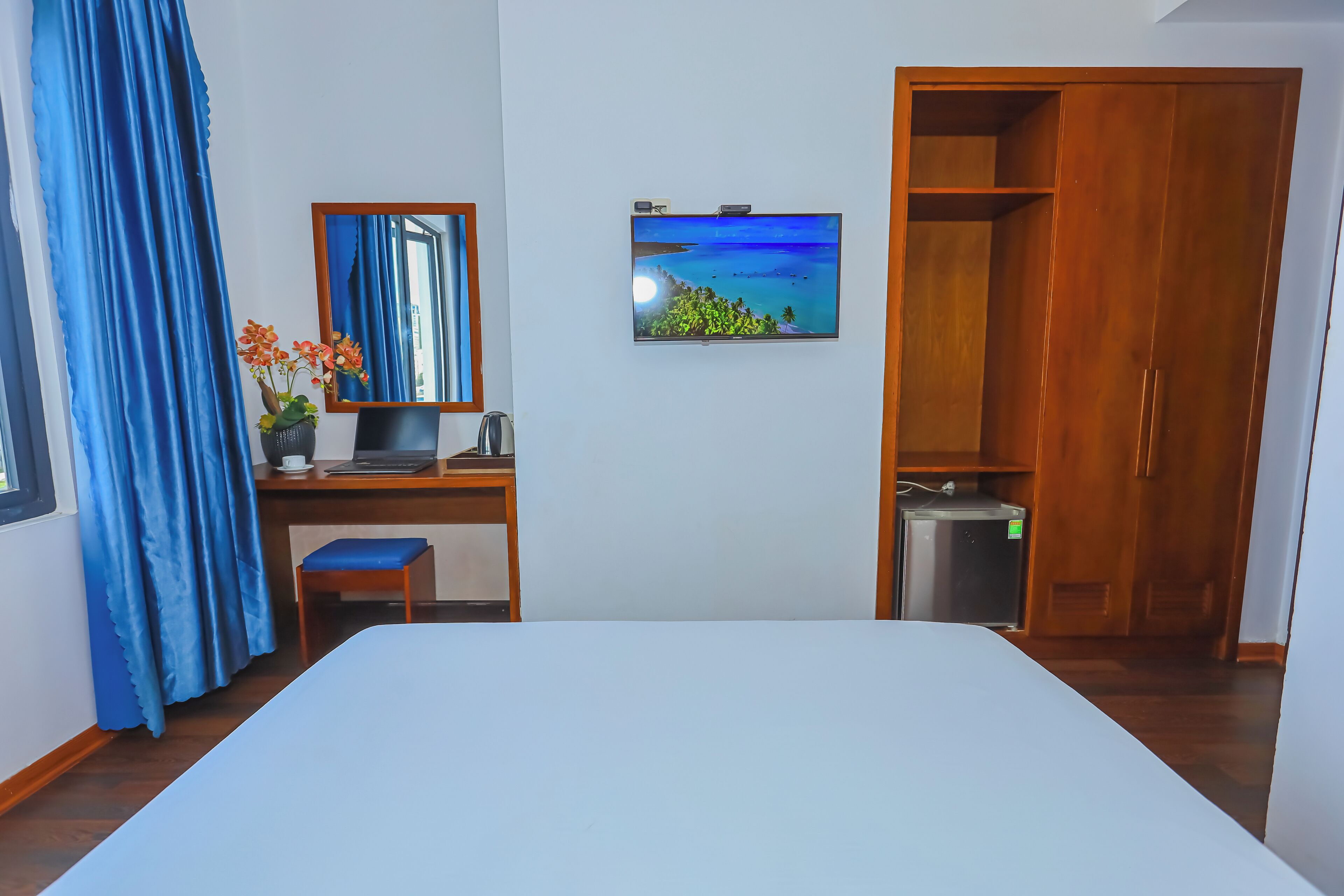 A bedroom with a bed, a desk with a computer, a TV, and a wardrobe.