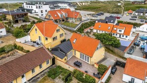 Una zona residencial costera con casas de techo rojo y una playa de arena, con vista al mar.