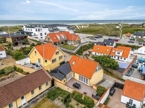 A coastal residential area with houses featuring red-tiled roofs, a sandy beach, and a view of the sea. - 4 Star Holiday Home in Lokken (Lokken)