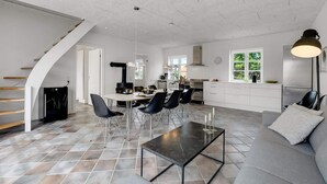 Una cocina moderna con una isla central, comedor con sillas, un sofá y una escalera.