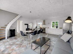 A modern kitchen with a central island, dining area with chairs, a sofa, and a staircase. - 4 Star Holiday Home in Lokken (Lokken)
