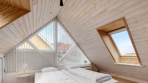 Un dormitorio con techo inclinado, una cama, una mesita y una ventana.