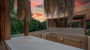 Una terraza con una mesa de hormigón, sillas de mimbre y vistas al atardecer.