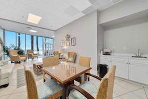 A modern dining area with wicker chairs, a glass-top table, and a view of the outdoors. - Admirals Quarters 708 | Beachfront Views | Luxury Amenities | Heart of Orange Beach (Orange Beach)