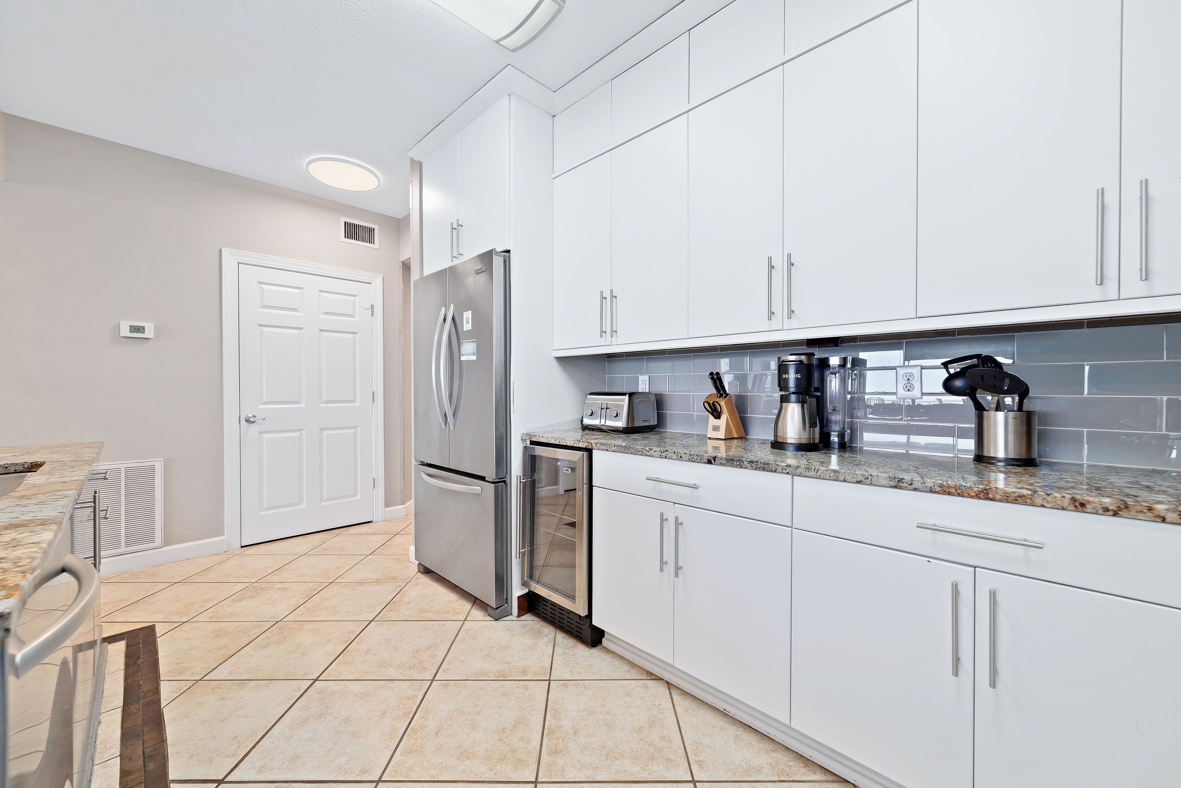 A modern kitchen with white cabinets, a stainless steel refrigerator, and a granite countertop.