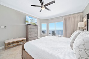 Ein Schlafzimmer mit einem großen Bett, einem Deckenventilator, einem Schminktisch, einem Fernseher und Meerblick durch das Fenster.