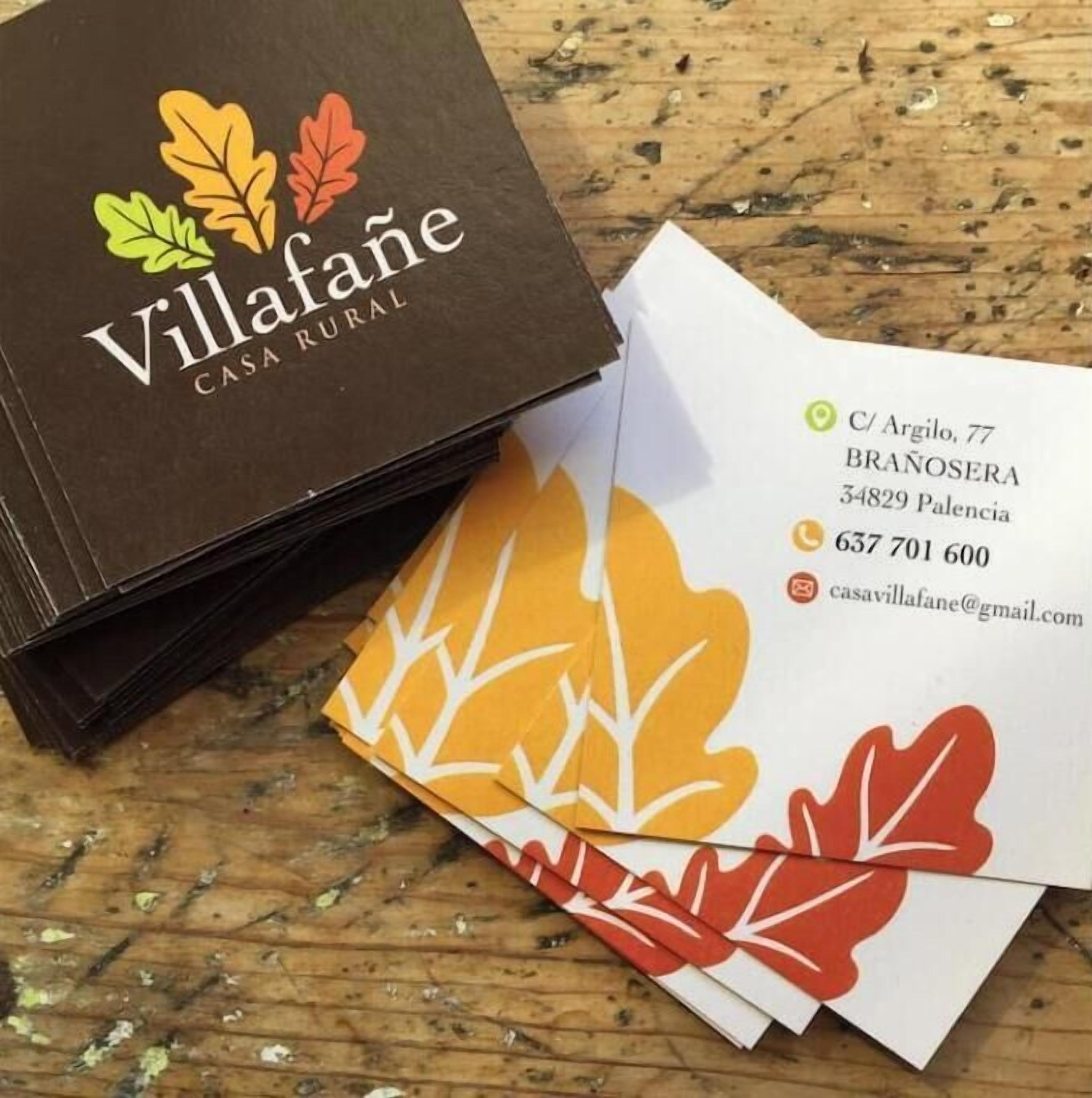 Un montón de tarjetas de visita marrones y un sobre blanco con un diseño de hoja, ambos con la etiqueta 'Villafane CASA RURAL'.