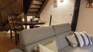 A living room with a sofa, striped pillows, a dining table with chairs, a wooden staircase, and a wall-mounted lamp. - Villafañe House (Brañosera)