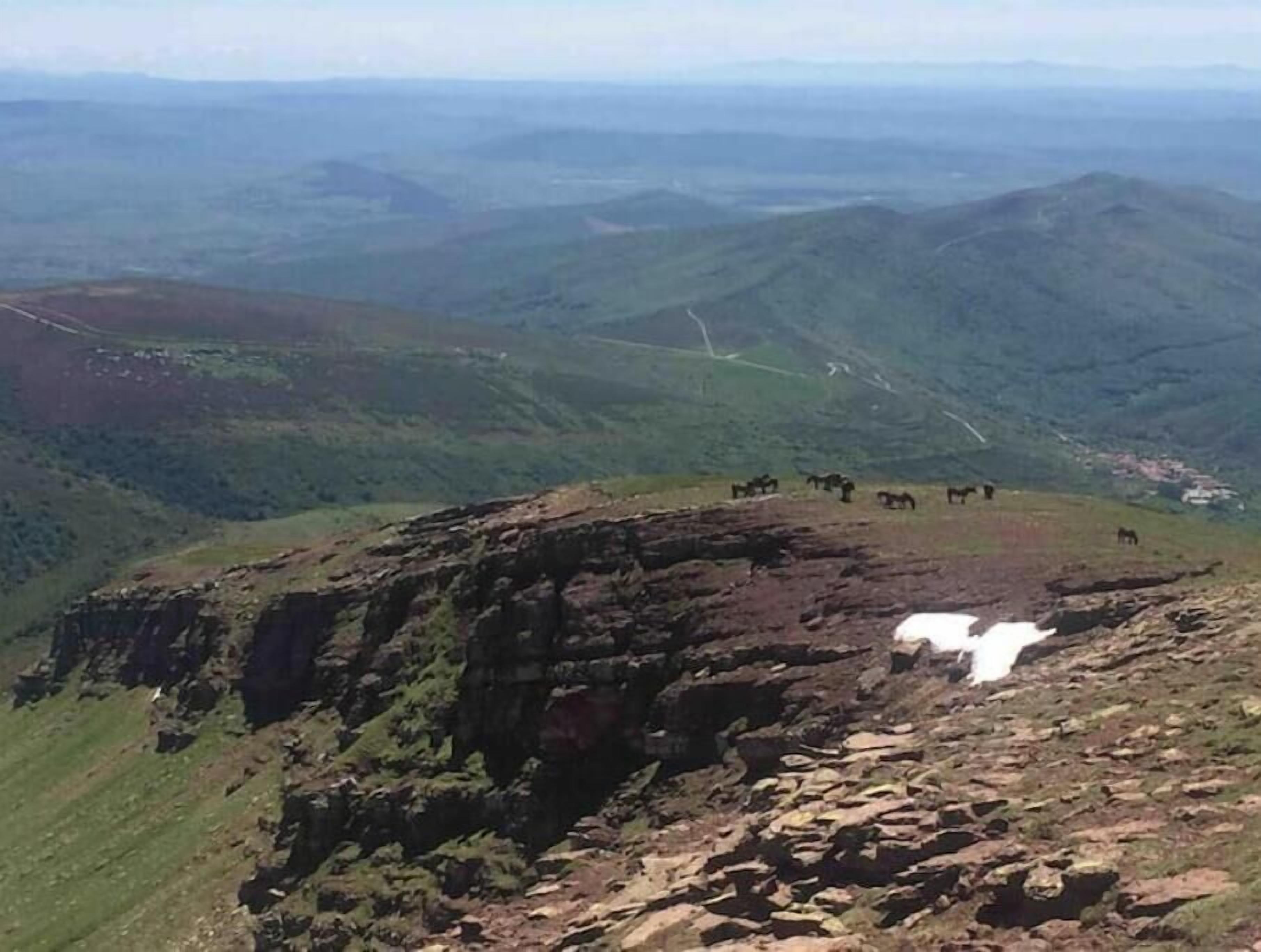 Un paysage montagneux avec une formation rocheuse et un troupeau de chevaux en train de paître.