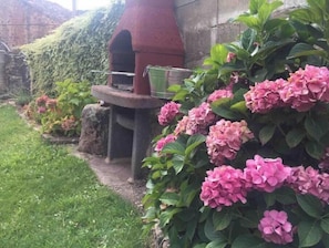 A garden with a brick oven, lush greenery, and pink hydrangea flowers.