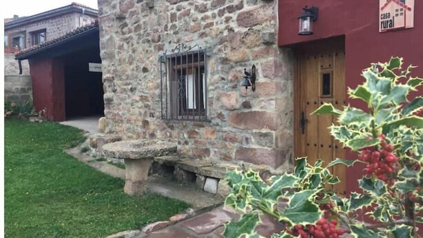 A stone building with a wooden door, a small porch, and a sign indicating it's a rural house. - Villafañe House (Brañosera)
