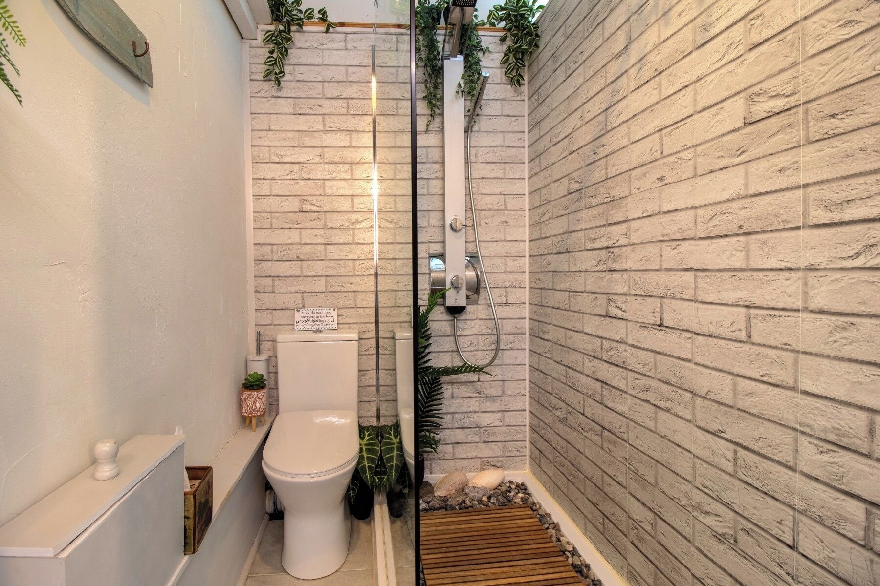 A bathroom with a white toilet, a shower with a glass door, and a brick wall.