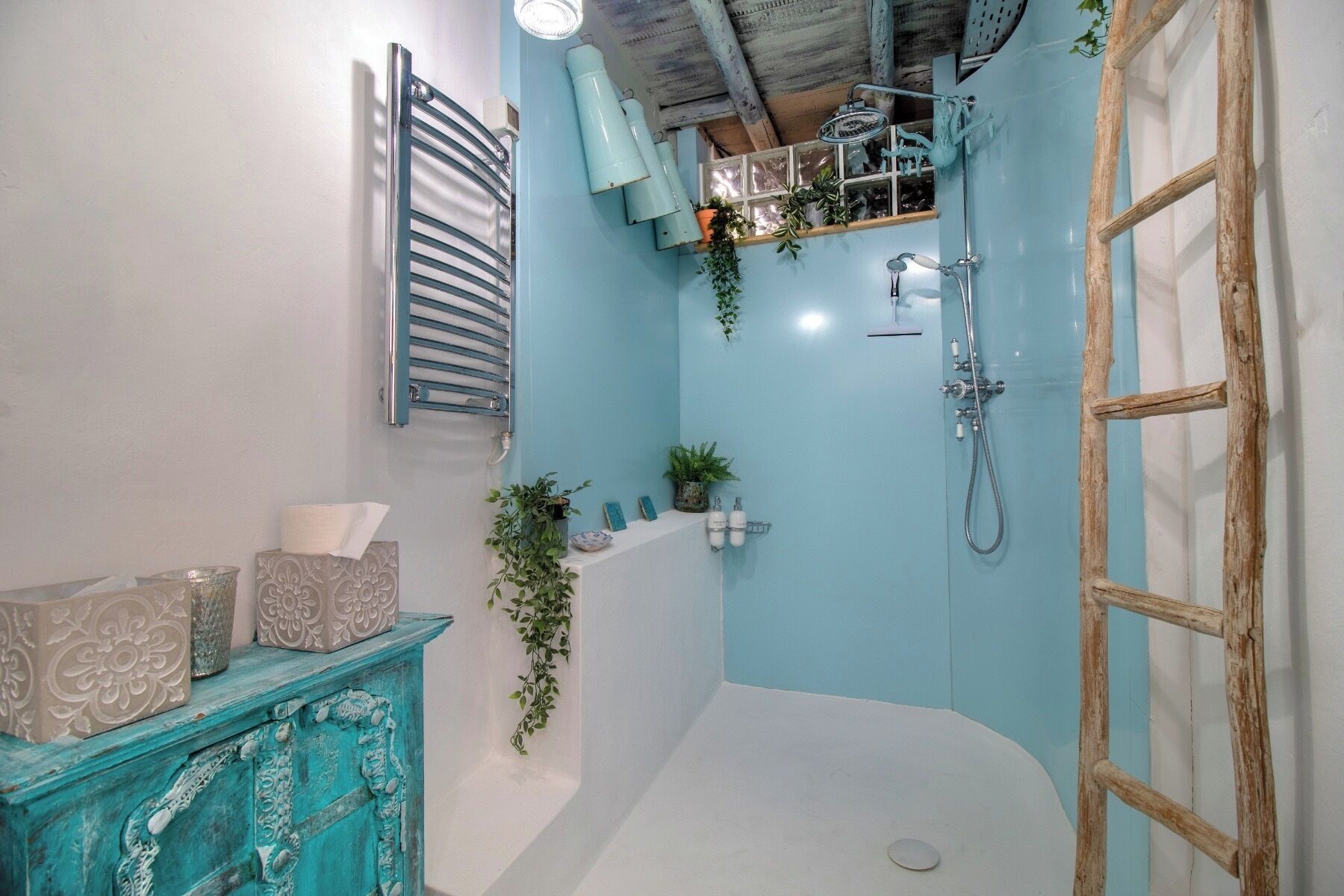 A bathroom with a blue wall, a wooden ladder, a shower, and a decorative cabinet.