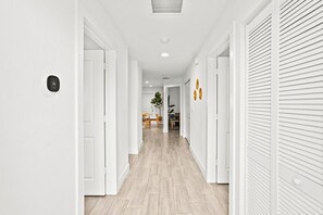 A hallway with white walls, a light wooden floor, and a door with a number plate. - Bright & Spacious 3BR | Close to Beaches (West Palm Beach)
