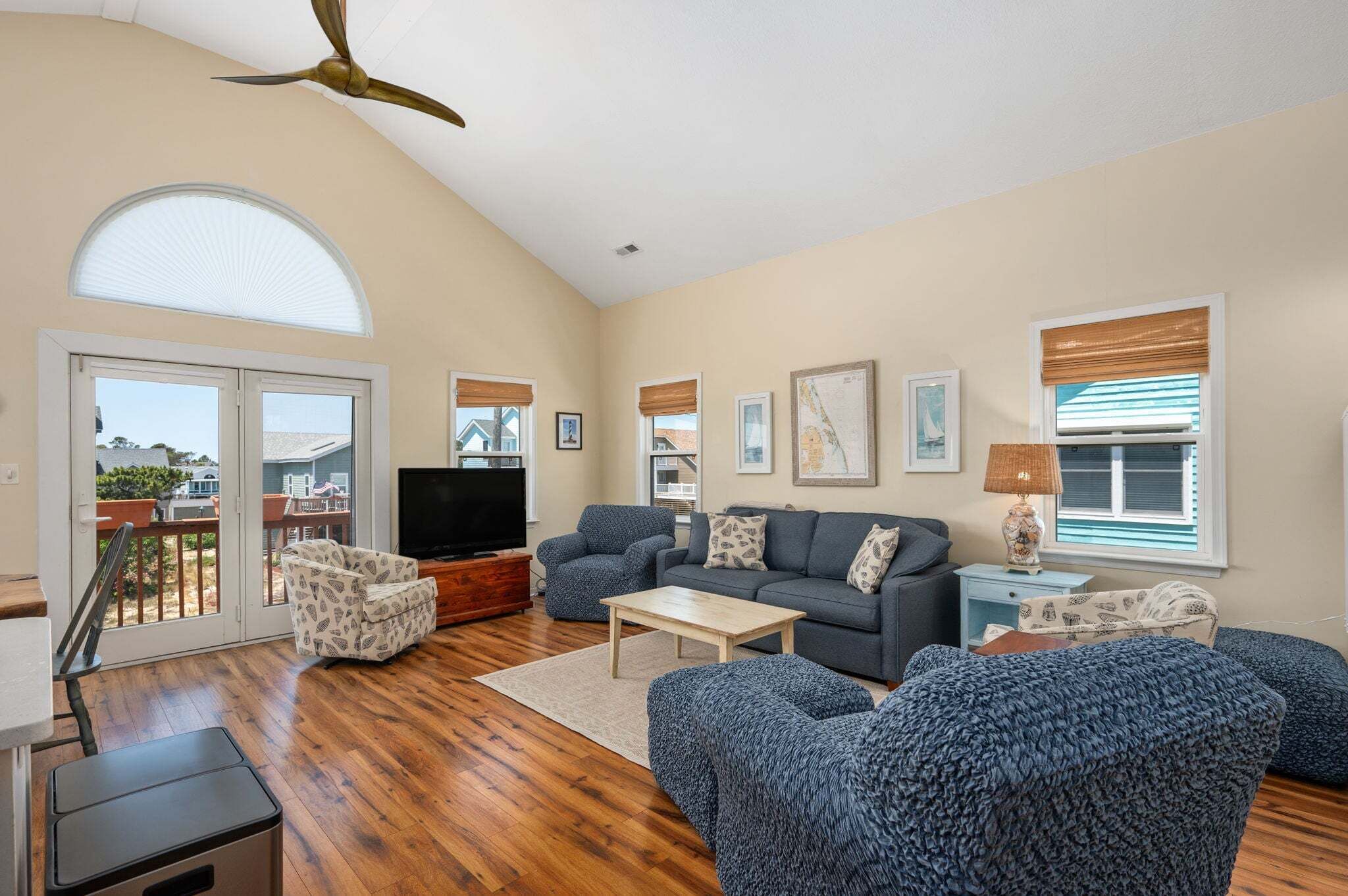 A spacious living room with a large TV, comfortable seating, and a balcony with a view.
