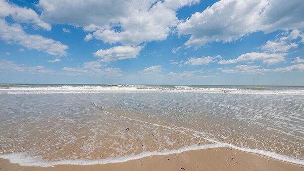 Een strand met een breed zandstrand en rustige golven.