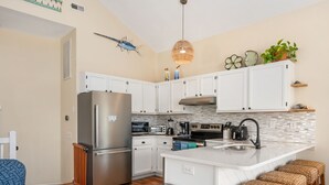 Een moderne keuken met witte kasten, roestvrijstalen apparatuur, een centraal kookeiland met barkrukken en decoratieve wandkunst.