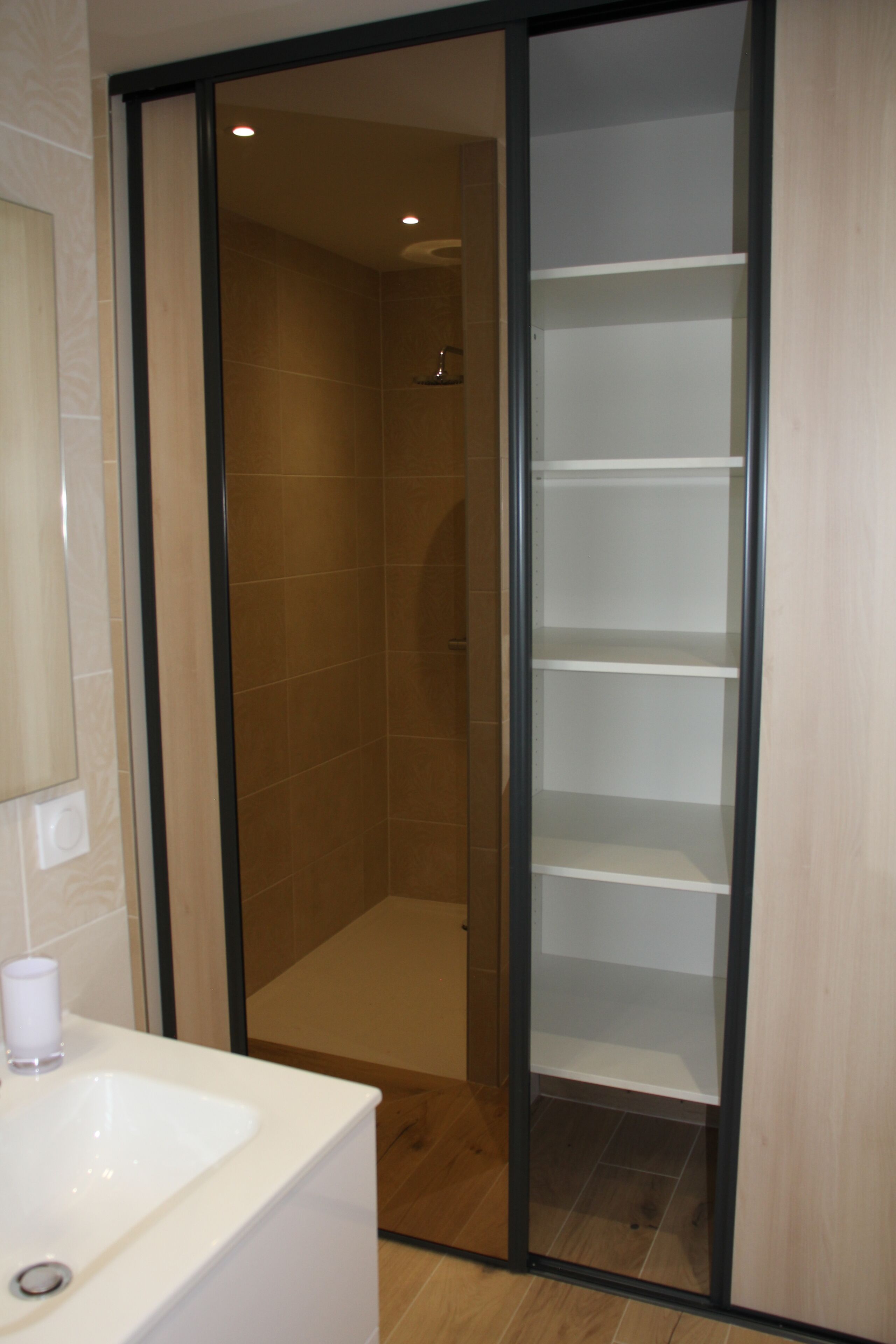 Un baño con lavamanos blanco, cabina de ducha de vidrio y suelo de madera.