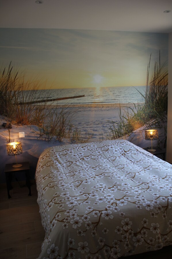 A bedroom with a beach mural, a bed with a floral bedspread, and two bedside lamps.