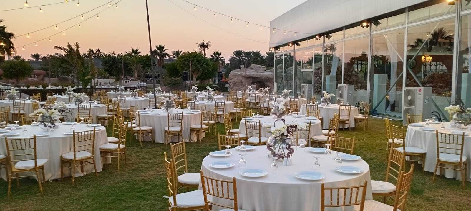 An outdoor event space with round tables, chairs, and string lights.