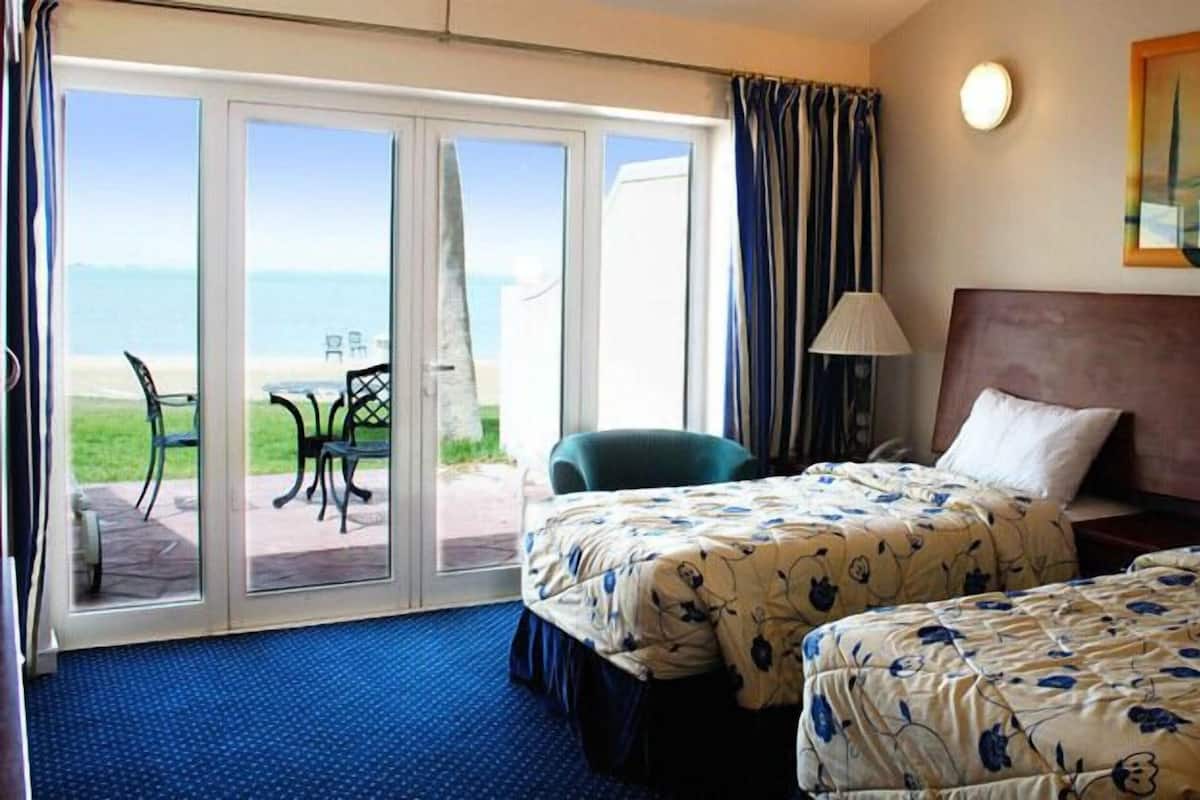 Habitación de hotel con dos camas, vista a la playa, una mesa y sillas afuera y obras de arte en la pared.