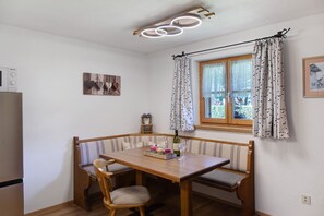 A dining area with a wooden table and bench, a window with patterned curtains, and a ceiling light fixture.