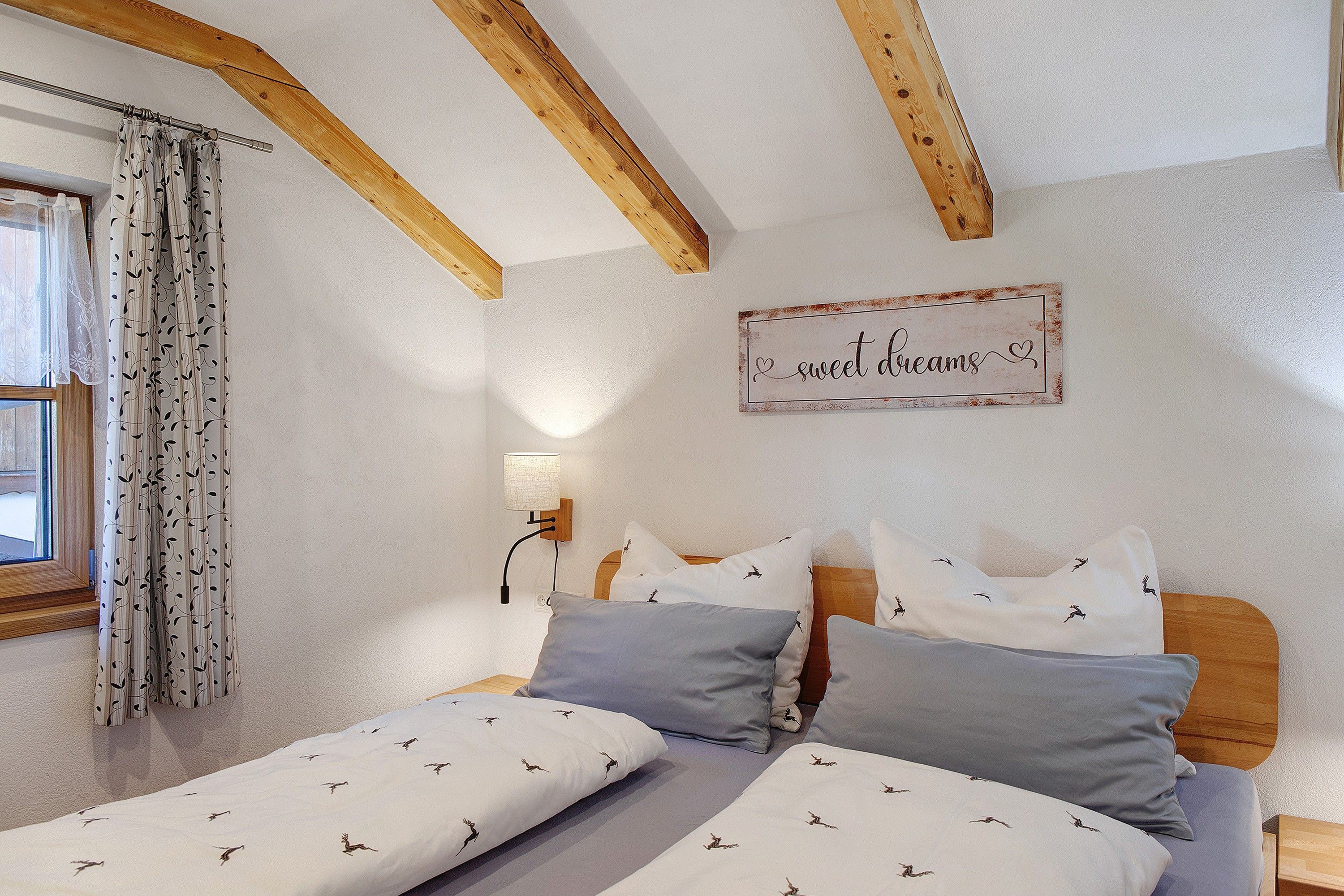 Ein Schlafzimmer mit Holzbalkendecke, einem Bett mit gemusterten Textilien, einer Wandlampe und einem dekorativen Schild.