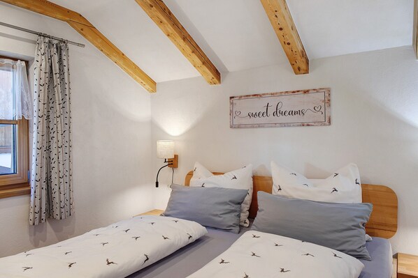 A bedroom with a wooden ceiling, a bed with patterned bedding, a wall-mounted lamp, and a decorative sign.