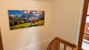 A painting of a mountain landscape with cows, a wooden staircase, and a window.
