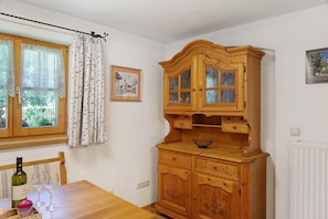 A wooden cabinet with glass doors, a dining table with wine glasses, and a window with curtains.