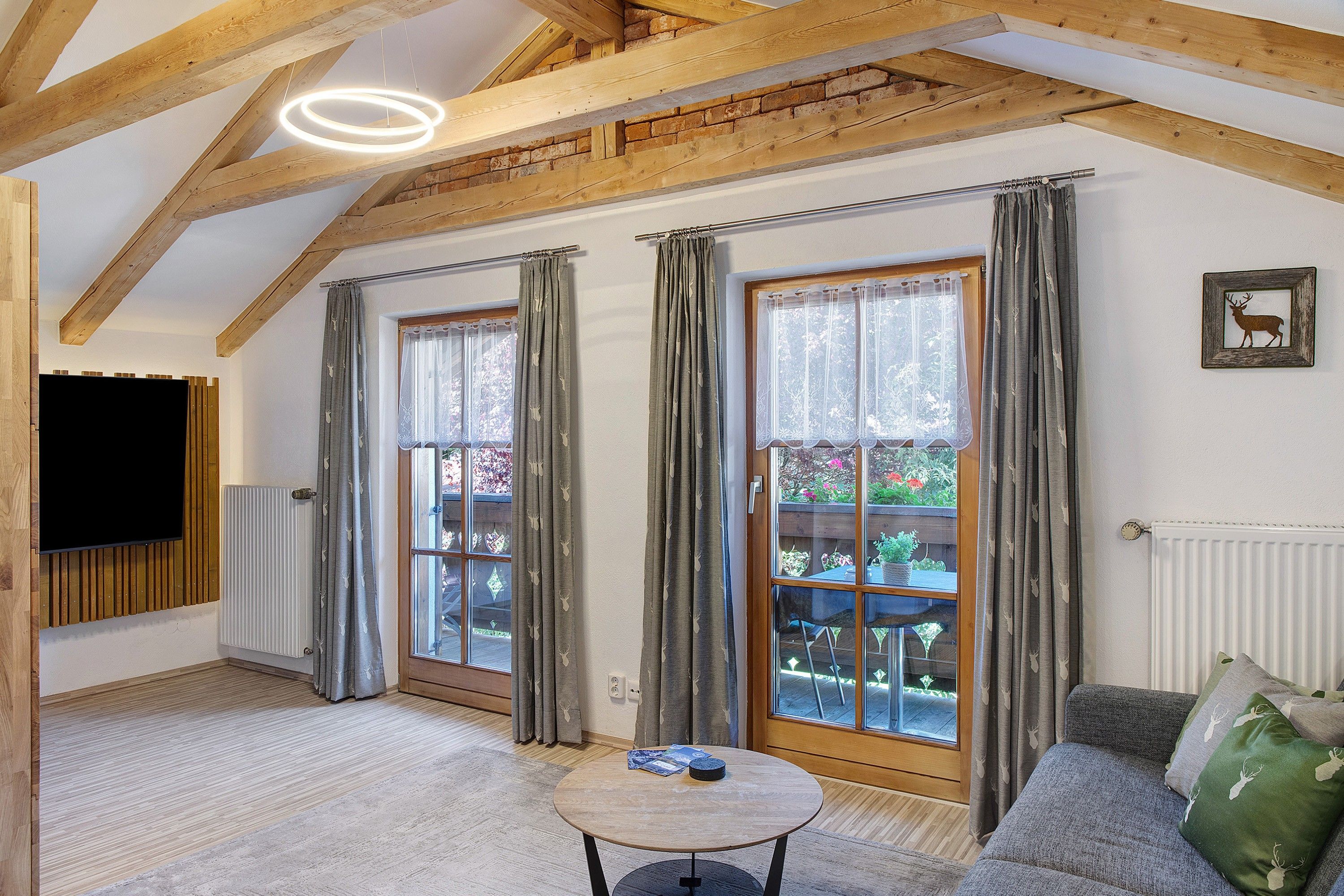A room with a wooden ceiling, a round table, a sofa, and a TV mounted on the wall.