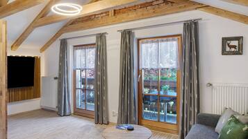 A room with a wooden ceiling, a round table, a sofa, and a TV mounted on the wall.